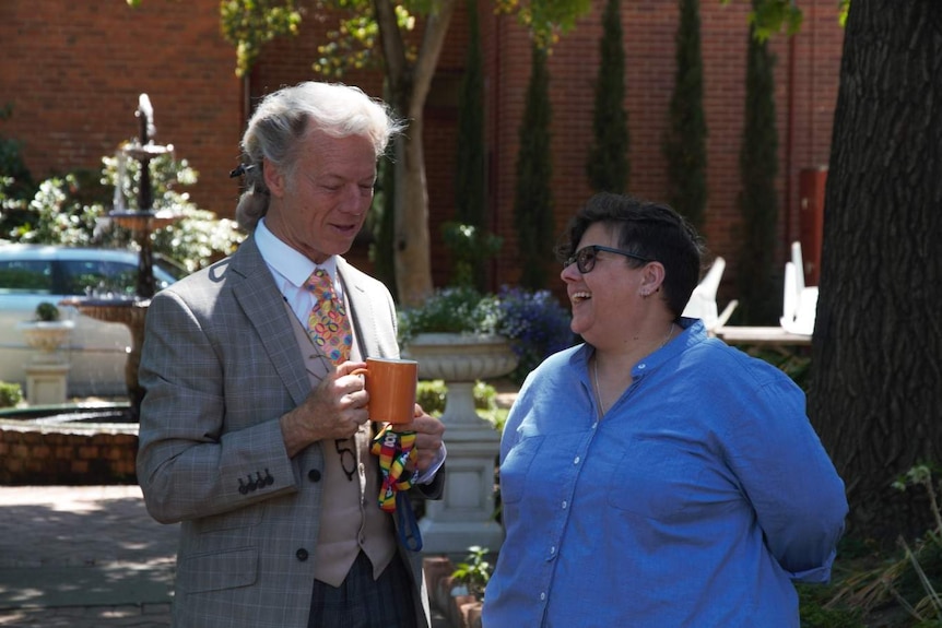 A priest and a woman laugh in a garden.