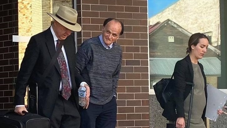 An elderly man exits court, a man and woman (his legal team) walk beside him.