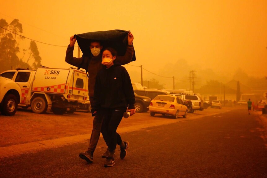 Two people walk under a jacket with masks under a smoky sky