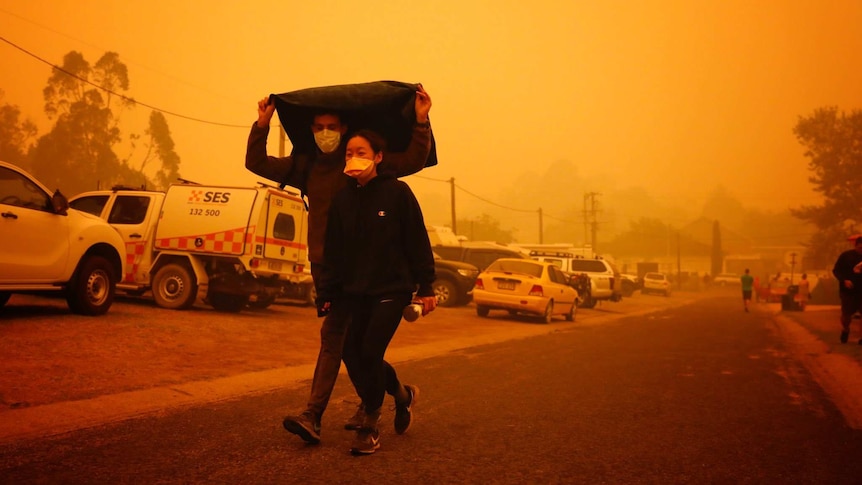 Two people walk under a jacket with masks under a smoky sky