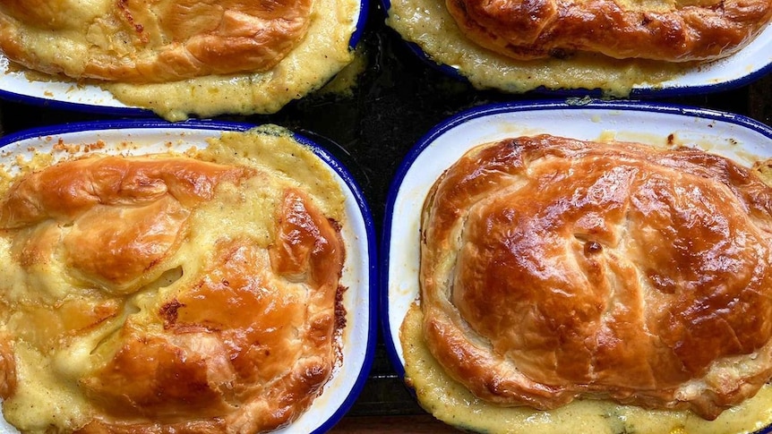 A photograph of four golden brown pies in small white and blue enamel tins.