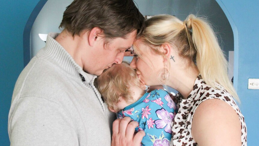 A man and a woman kiss a small child's head.
