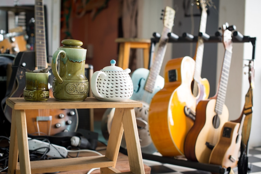A number of teapots and teacups placed on a short stool in front of a range of musical instruments.