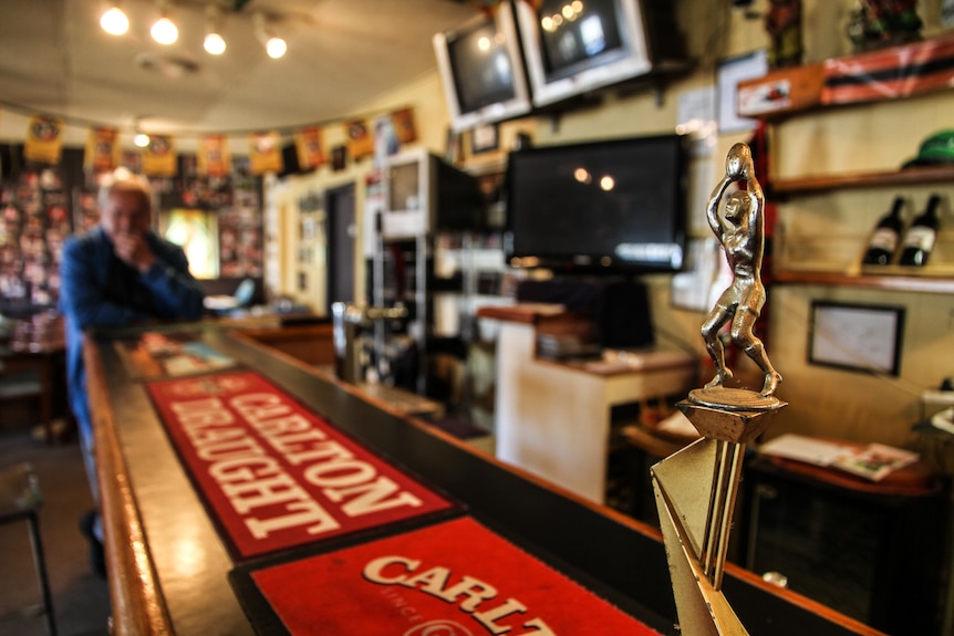 A football trophy sits on the bar, televisions and wine bottles on the wall behind.