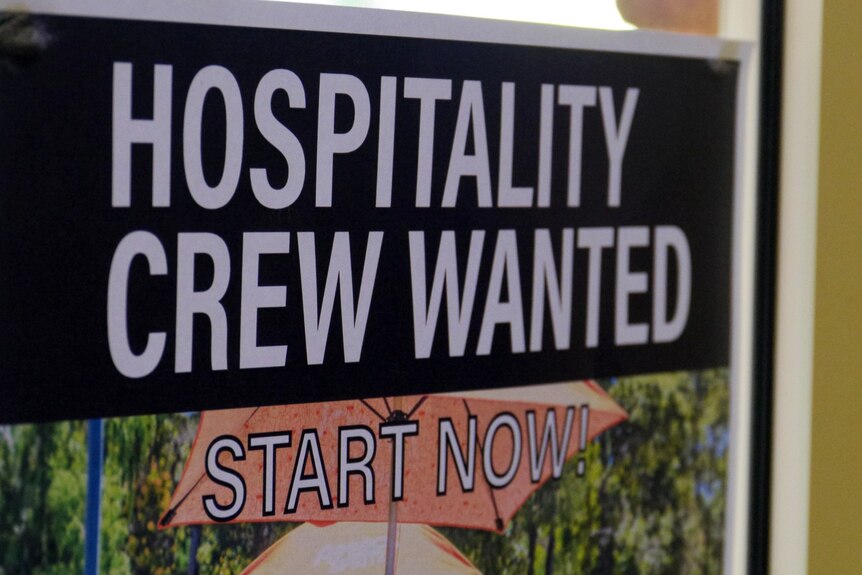 A sign in a window reading 'hospitality crew wanted - start now'
