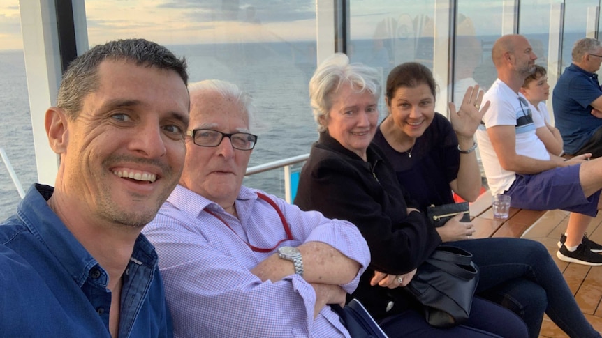 Four adults sit against a glass window overlooking the ocean on a cruise ship.