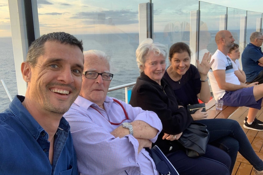 Four adults sit against a glass window overlooking the ocean on a cruise ship.