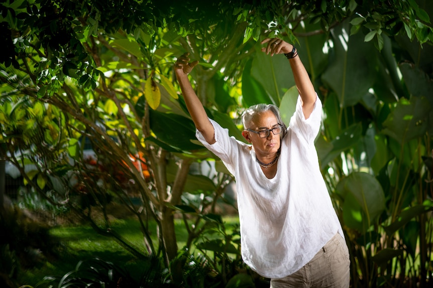 A man in a white shirt is outside performing dance moves.