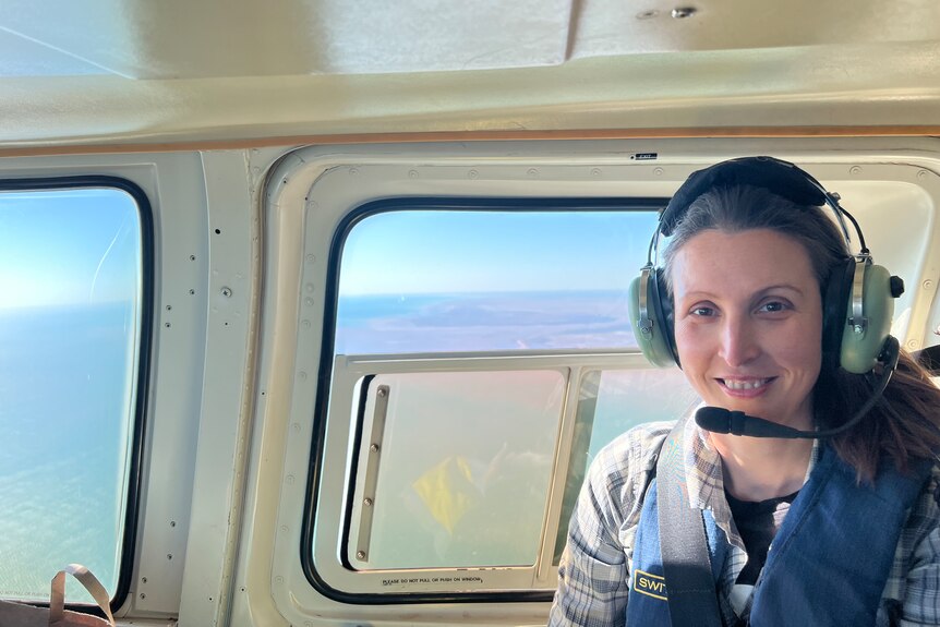A close of shot of a woman in a head set sitting near a helicopter window