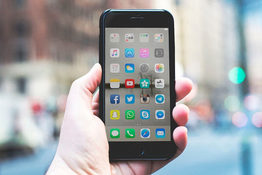 Hand holds up a smartphone mobile with home screen display.