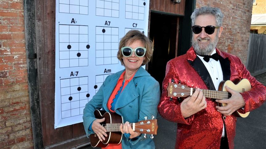 A man and a woman in sunglasses each holding a ukulele and smiling at the camera.