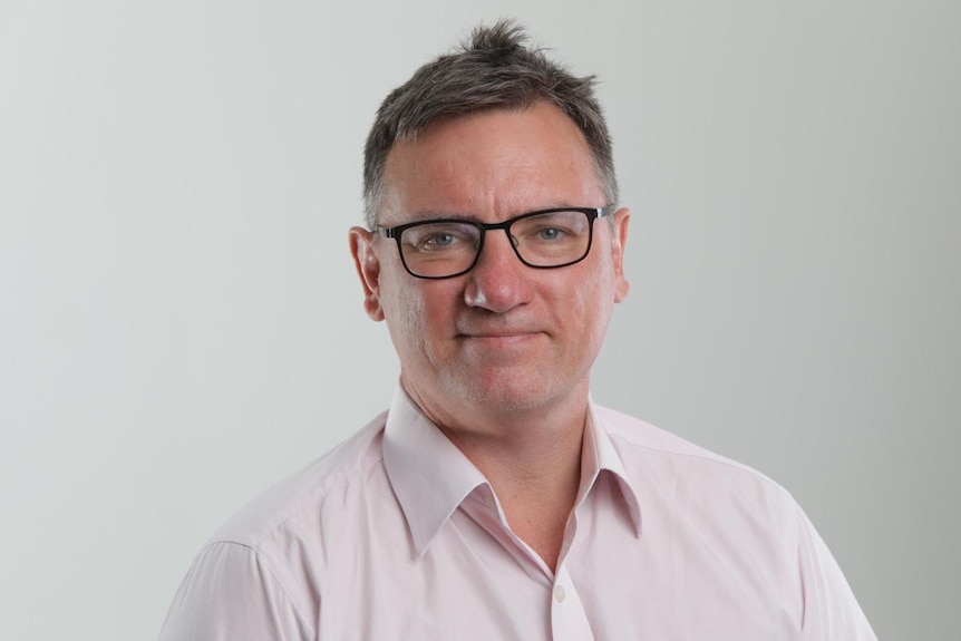 A middle-aged man wearing a light-coloured shirt and glasses.