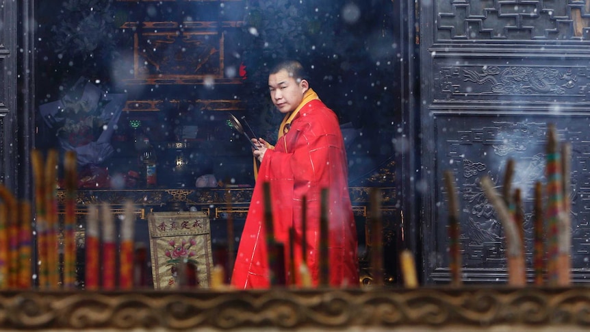 A monk is seen through an incense burner inside a temple as snow falls in Jiaxing, Zhejiang province, China