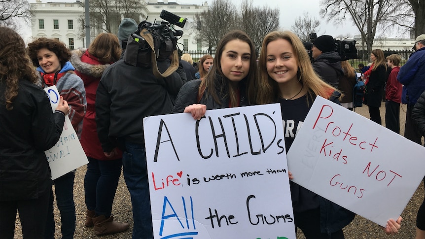 Two young women stand in front of the White House holding  gun control reform placards.