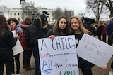 Two young women stand in front of the White House holding  gun control reform placards.