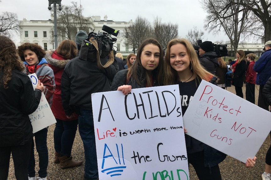 Two young women stand in front of the White House holding  gun control reform placards.