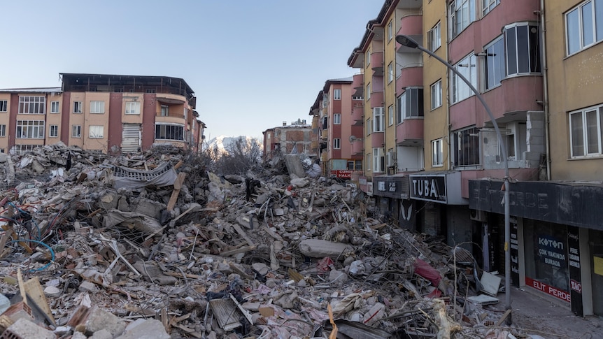 Piles of concrete and rubble alongside apartment buildings and shops still standing. 