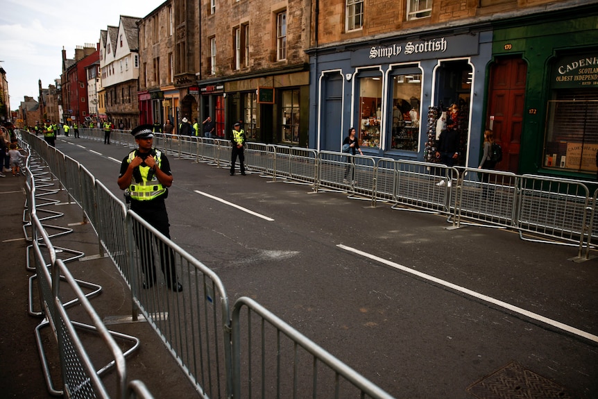 Police in hi-vis patrol a street which is blocked off by metal railings.