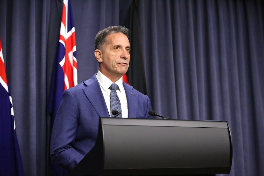 A man wearing a blue suit and tie stands behind a lecturn