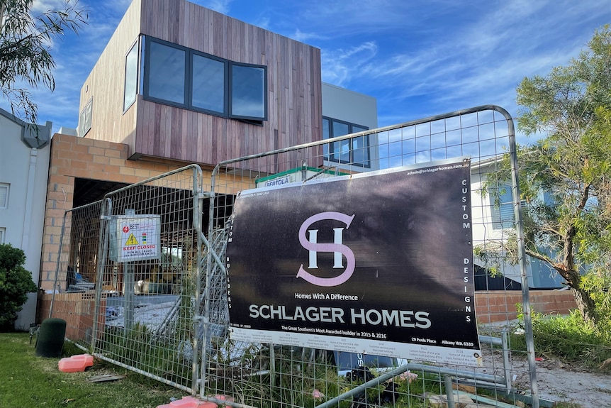 A sign saying Schlager Homes outside a wire fence and a partially built house