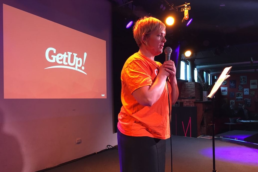 A woman stands on stage speaking into a microphone