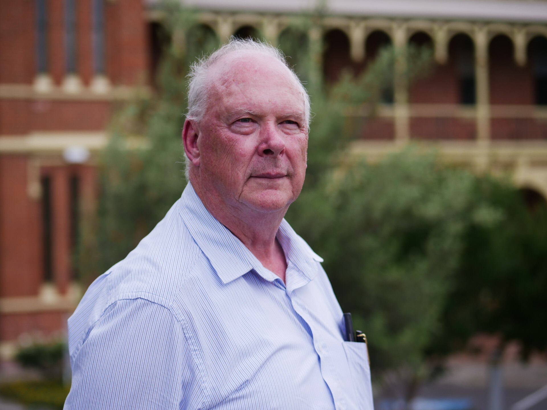 A man in a business shirt standing in front of an old hospital building
