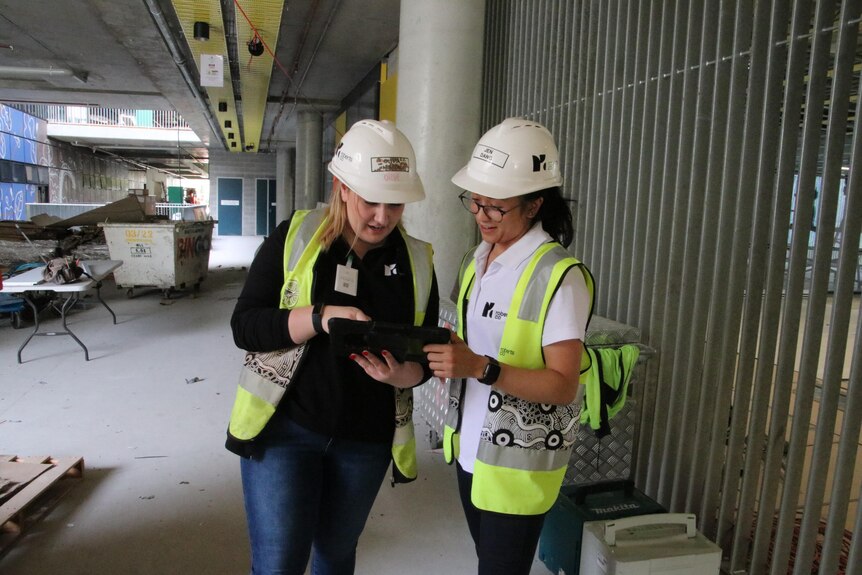 two wome wearing hard hats looking at file