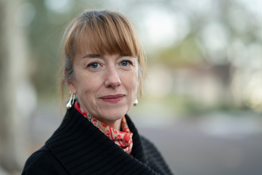 Woman wearing black cardigan and red scarf smiles.