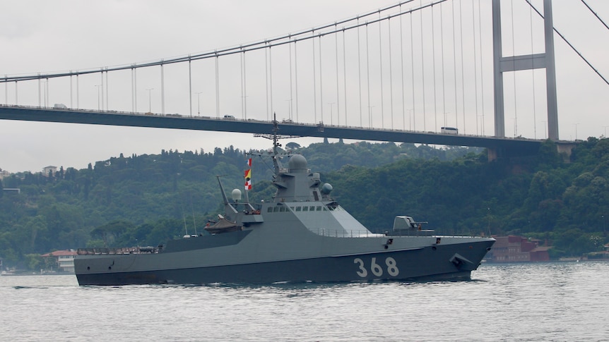 A grey navy patrol ship with a bridge in the background. 