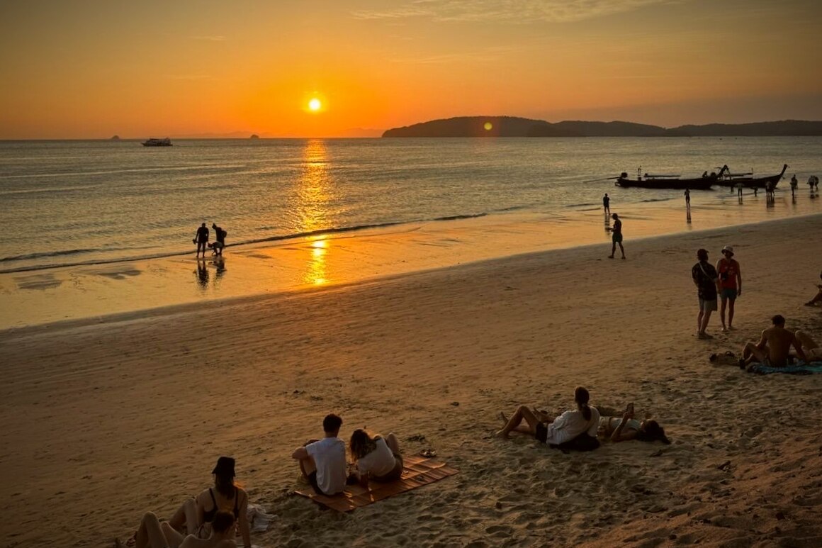 A sunset over a beach with people lounging on the shore