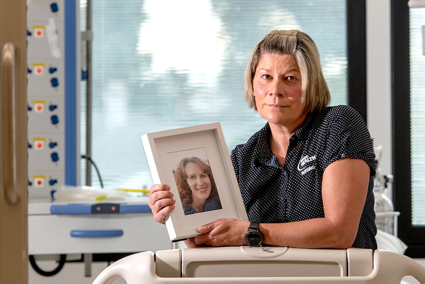 woman in a nurses uniform, sitting on a bed, holding a frame with a photo of her sister who looks friendly and kind