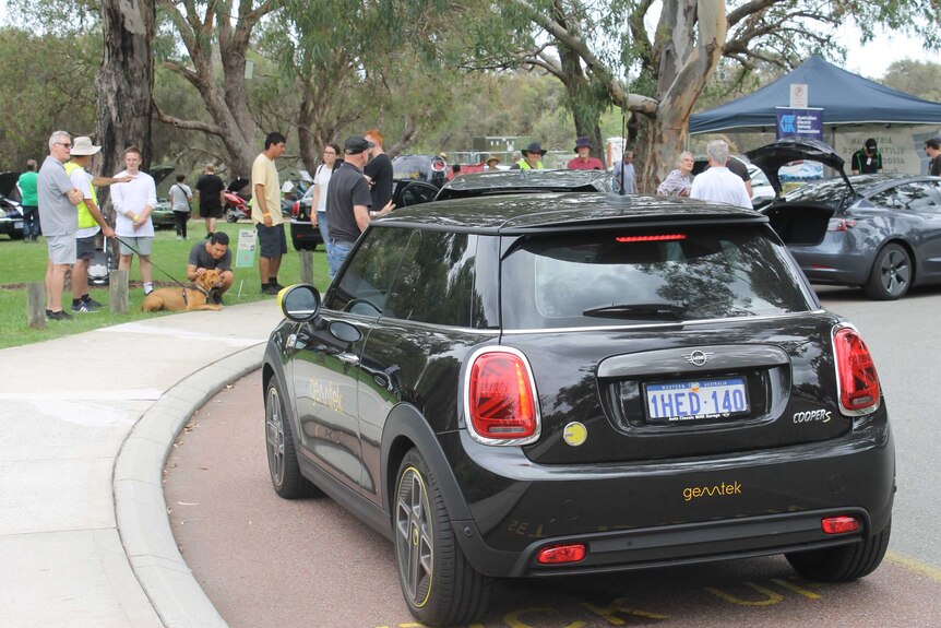 A black electric mini in the foreground, with people at the expo in the background