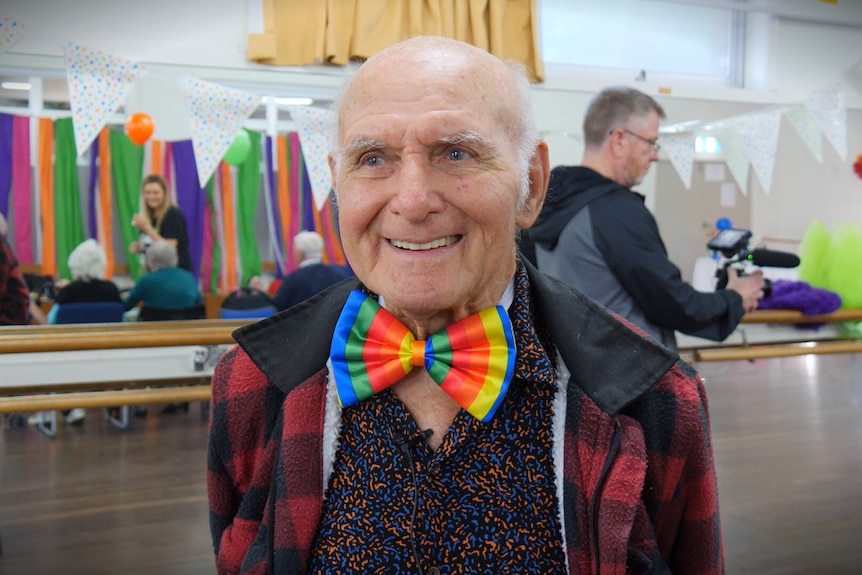 A man in aged care, wearing a rainbow-coloured bow tie, talks about the joy he gets from dancing