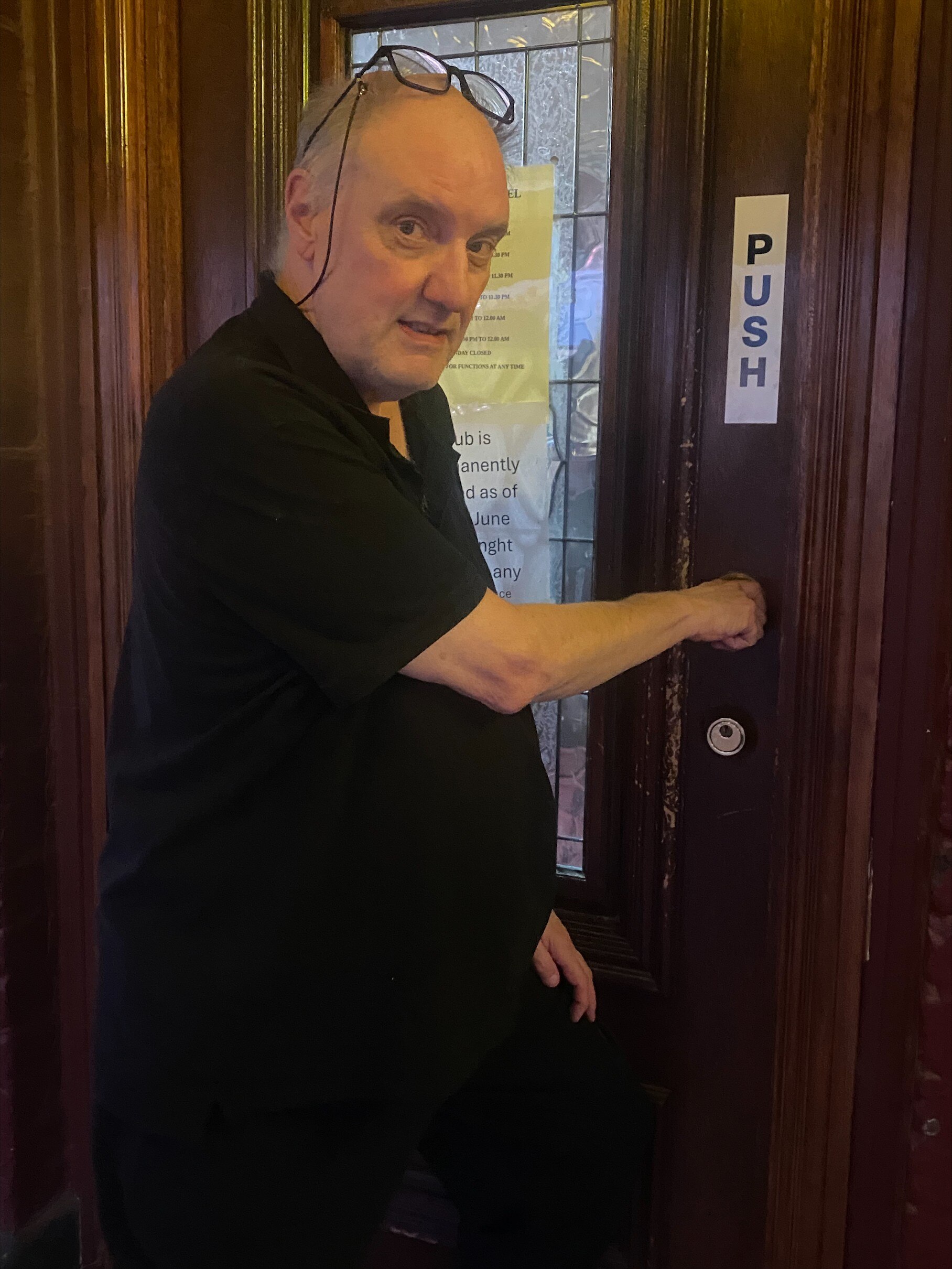 Grant, a man with his hand on a wooden door with glass panneling, looking over his shoulder at the camera.