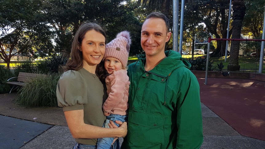 A photo of a woman holding a baby standing next to a man. 