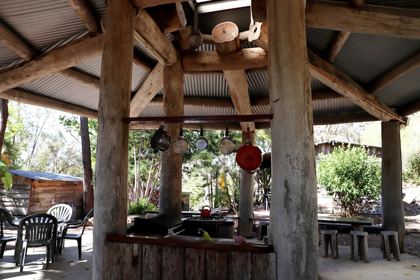 A kitchen housed under a high sloping tin roof with big timbre logs supporting it, filled with natural light.