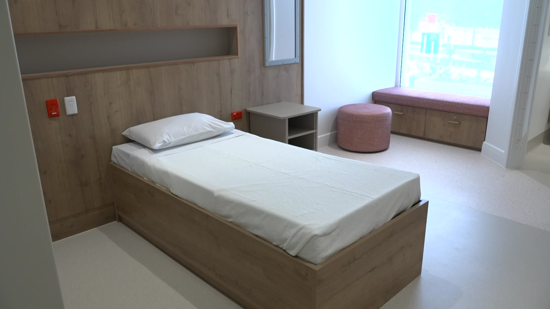 Una cama recién hecha con sábanas blancas en una habitación de hospital vacía con una ventana grande