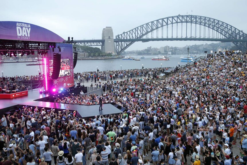 A large crowd watches a concert performed with the Sydney Harbour Bridge in the background.