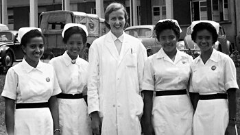 A women in a white doctor's coat poses with four nurses in a black and white photo