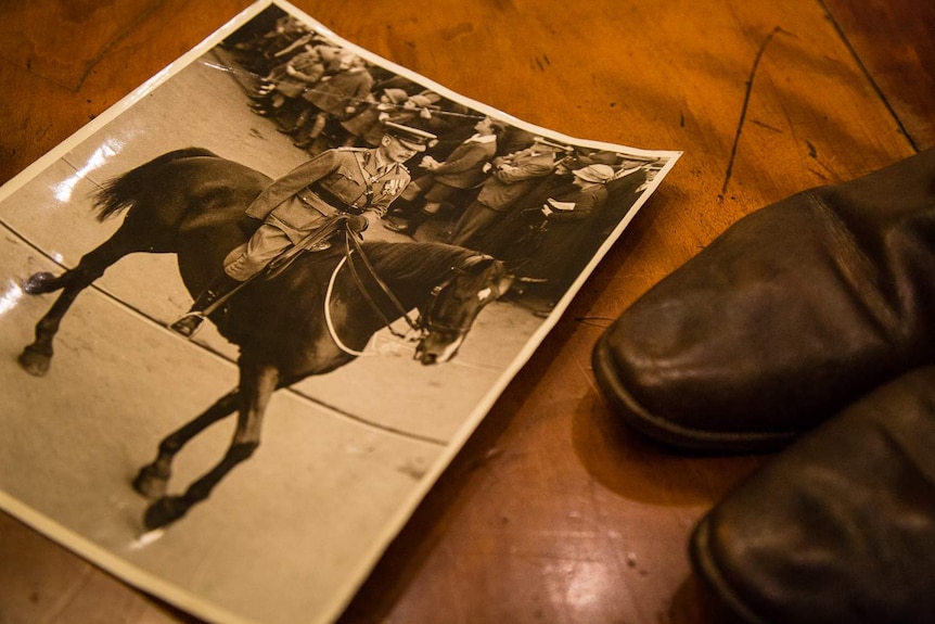 A photograph of Walter Cass leading the funeral procession for Sir John Monash sits on a table with a pair of  boots.