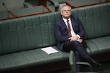 Morrison is sitting on the front bench by himself, looking upwards in a reflective pose.