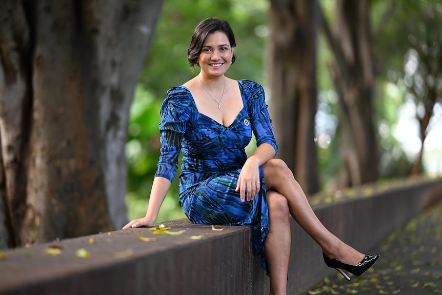 A woman sits outside wearing a blue dress and smiling for a photo,