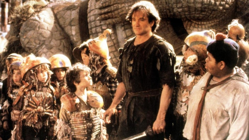 An image of a man with long, messy hair, in bedraggled clothes and holding a sword, surrounded by children ready for battle.