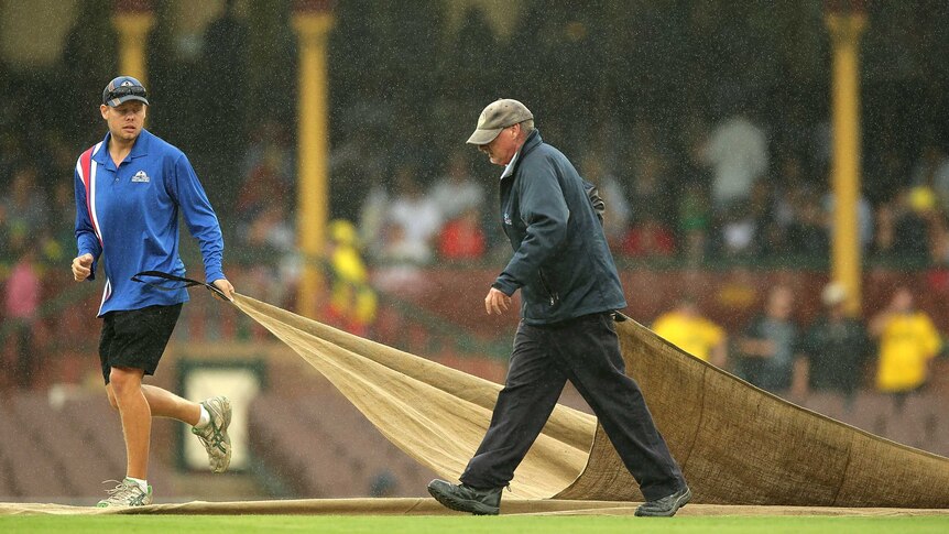 Groundsmen pull the covers on the SCG pitch as rain falls