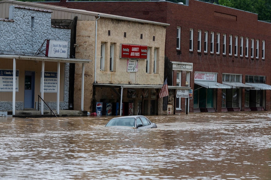 Un automóvil sumergido en aguas profundas de inundación en medio de una calle de la ciudad.