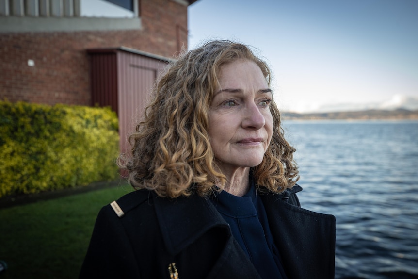 A woman looks seriously to the side of the camera, gazing out over water.