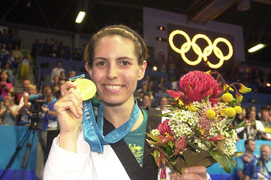 A woman holds up her gold medal at the Olympics and smiles.