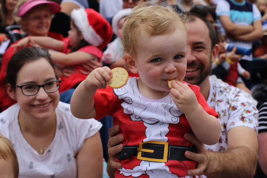 A baby wearing a Santa suit enjoying the Christmas pageant