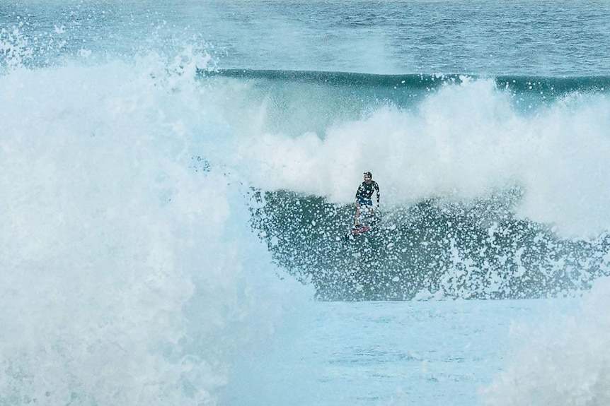 A surfer in white water in front of a large wave