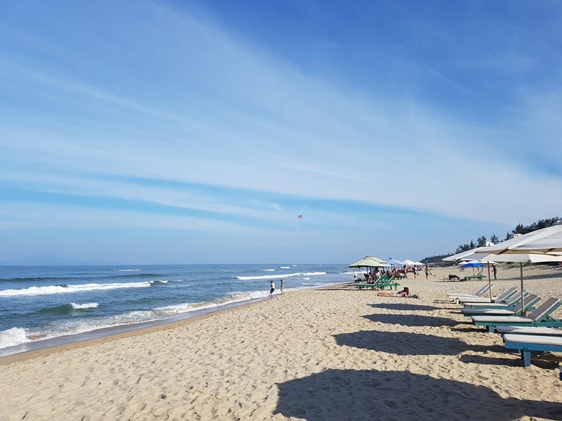 A woman's knees in the shade looking out over the beach and water.